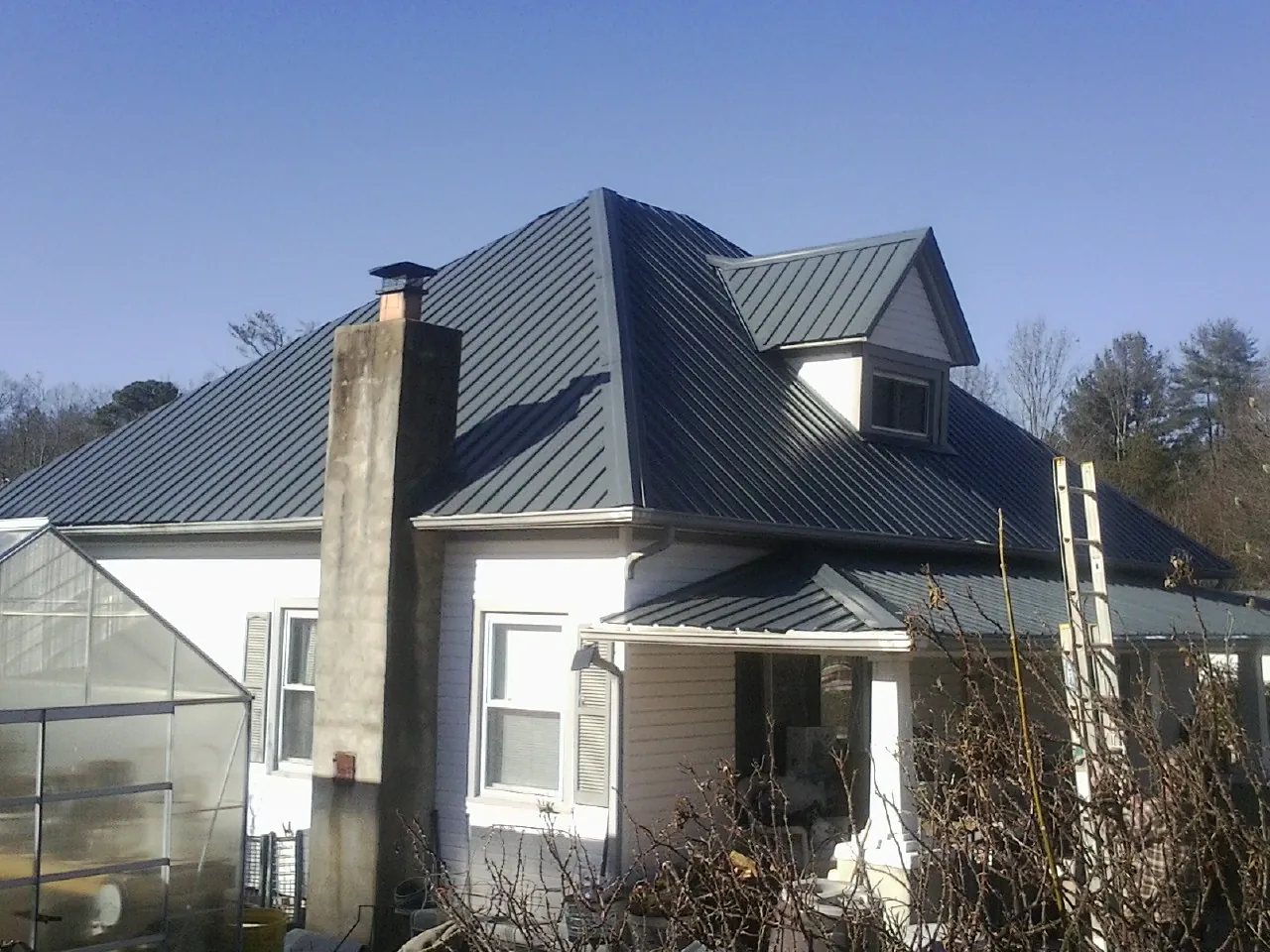 Dark blue standing seam metal roof on a white farmhouse with dormer — Slate & Tile Roof Repair by Roofing Brothers in Latah