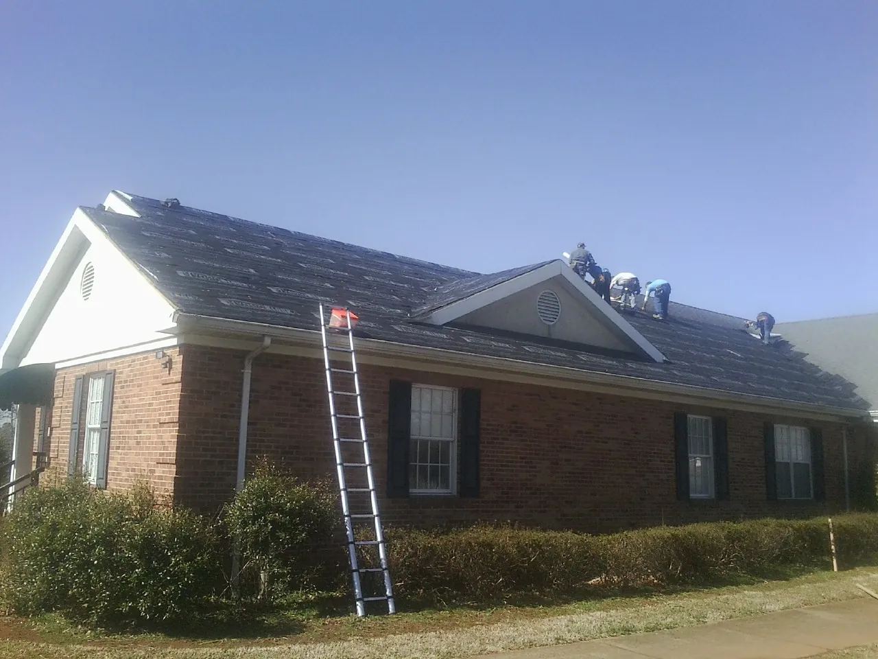 Crew tearing shingles off a brick ranch roof with a ladder set — Emergency Roof Repair work by our crew in Latah