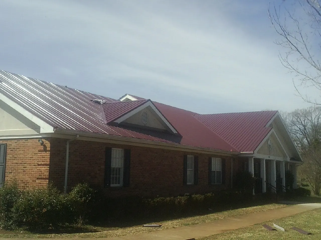Red metal roof with gabled entries on a long brick building, from a Hail Damage Roof Repair job in Latah