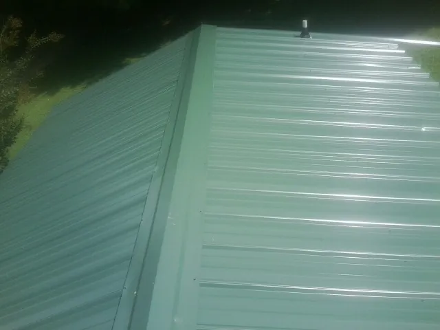 New green metal panels meeting at the ridge of a roof — Flat Roof Repair work by our crew in Latah