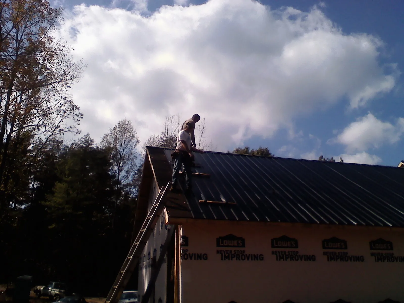 Roofer fastening dark metal panels high against a cloudy sky, from a Roof Inspection job in Latah