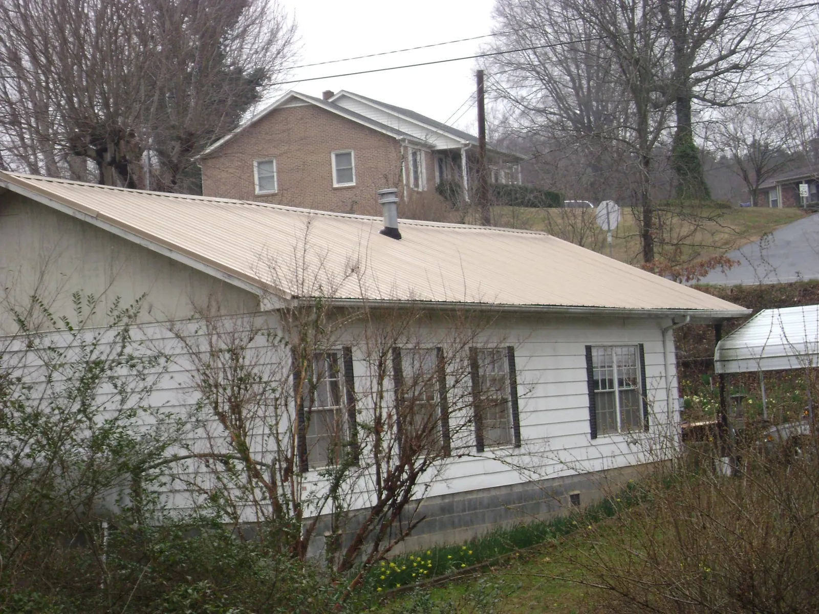 Tan metal roof on a white sided house set into a hillside — Commercial Roofing by Roofing Brothers in Latah